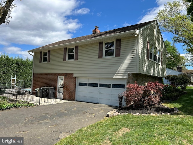 view of side of home featuring a garage, a chimney, aphalt driveway, brick siding, and fence