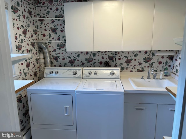 washroom with a sink, cabinet space, wallpapered walls, and washer and clothes dryer