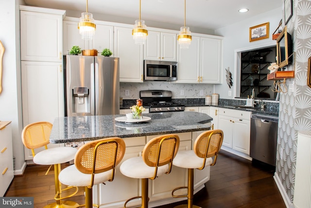 kitchen with decorative backsplash, appliances with stainless steel finishes, a center island, white cabinetry, and dark wood-type flooring