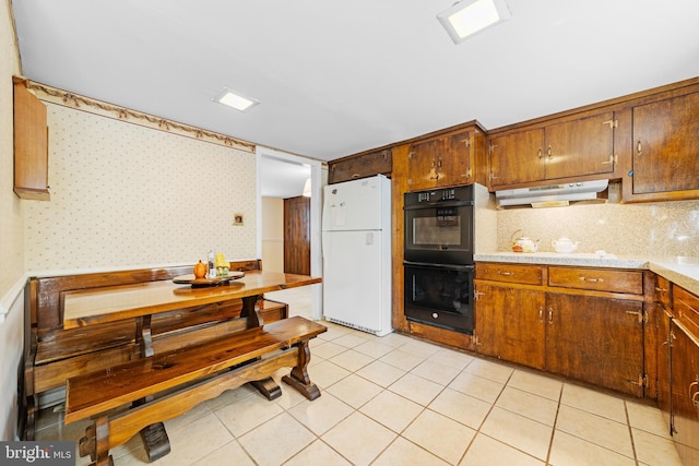 kitchen with dobule oven black, light countertops, freestanding refrigerator, under cabinet range hood, and wallpapered walls