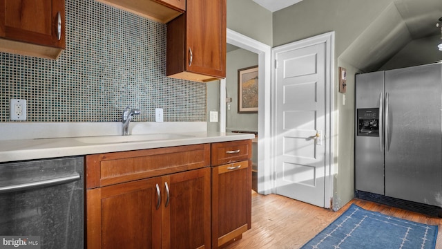 kitchen with brown cabinetry, light countertops, a sink, light wood finished floors, and stainless steel appliances