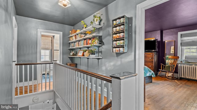 hallway with radiator heating unit, wood finished floors, and an upstairs landing