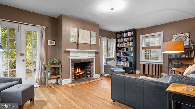 living room featuring radiator, baseboards, a brick fireplace, and wood finished floors