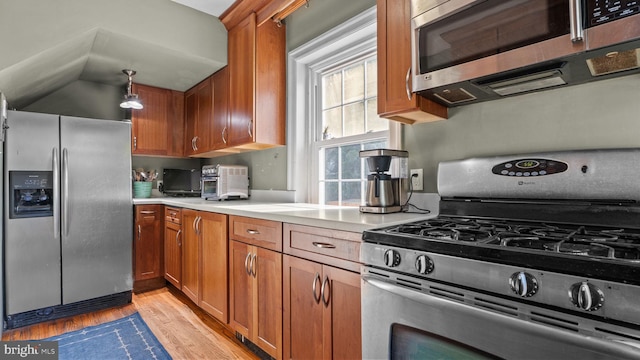 kitchen featuring light countertops, appliances with stainless steel finishes, light wood finished floors, and brown cabinets