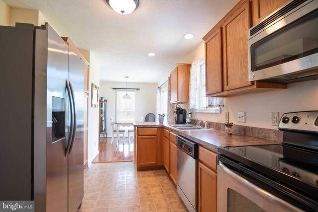 kitchen with recessed lighting, appliances with stainless steel finishes, brown cabinets, a sink, and a peninsula