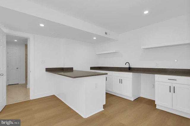 kitchen featuring light wood-type flooring, dark countertops, open shelves, and white cabinetry