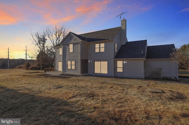 back of property at dusk with a yard and a chimney