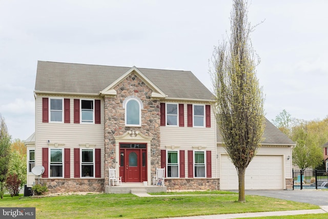 colonial house with a front lawn, driveway, stone siding, and an attached garage