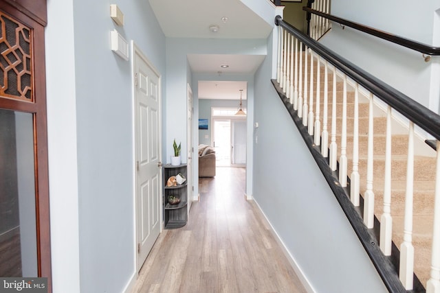 hall with light wood finished floors, stairway, and baseboards