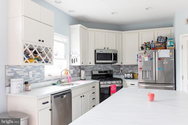 kitchen with tasteful backsplash, white cabinets, a sink, appliances with stainless steel finishes, and light countertops