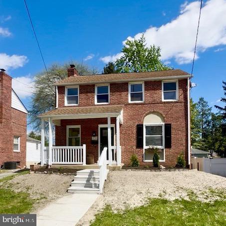view of front of home with a chimney, brick siding, a porch, and fence