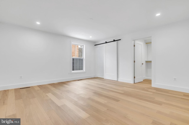 unfurnished bedroom with visible vents, baseboards, recessed lighting, a barn door, and light wood-style flooring