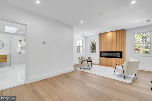 unfurnished room with a fireplace, light wood-style flooring, recessed lighting, a skylight, and visible vents