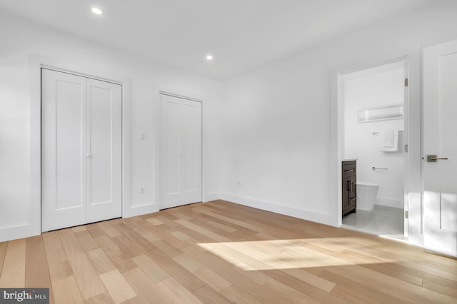unfurnished bedroom with recessed lighting, light wood finished floors, multiple closets, and ensuite bath