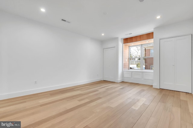 unfurnished bedroom featuring light wood-style floors, recessed lighting, baseboards, and two closets