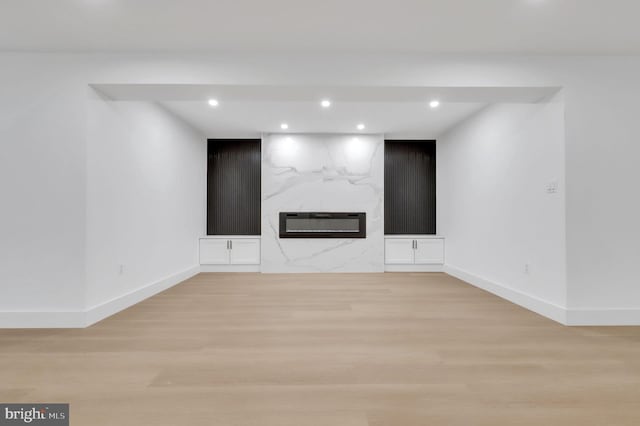 unfurnished living room featuring recessed lighting, baseboards, a high end fireplace, and light wood-type flooring
