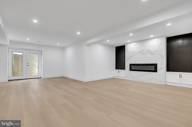 unfurnished living room featuring french doors, a high end fireplace, light wood-type flooring, baseboards, and recessed lighting