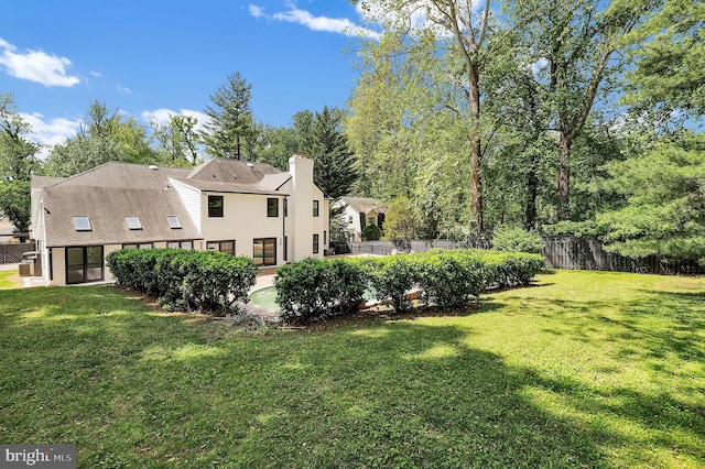 rear view of property with fence, a chimney, a lawn, and stucco siding