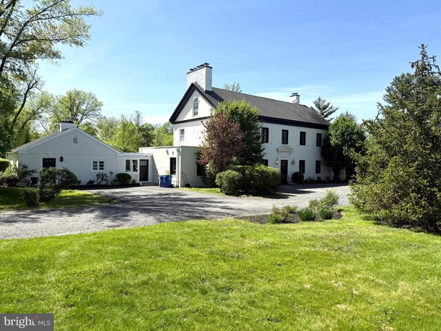 view of front of property featuring curved driveway, a chimney, and a front yard