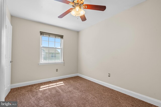 empty room with carpet flooring, ceiling fan, visible vents, and baseboards