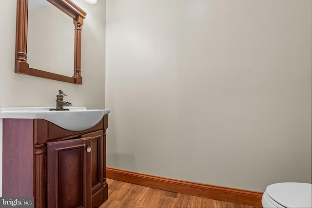half bath with baseboards, wood finished floors, toilet, and vanity