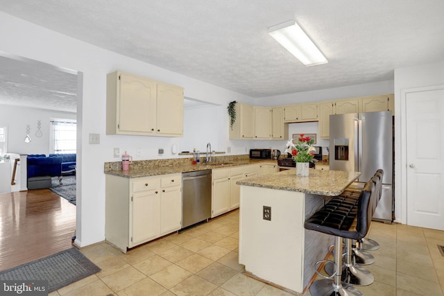 kitchen with a center island, a sink, stainless steel appliances, a kitchen breakfast bar, and a textured ceiling