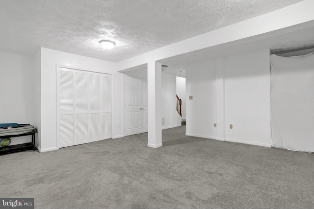 finished below grade area with carpet, a textured ceiling, baseboards, and stairs