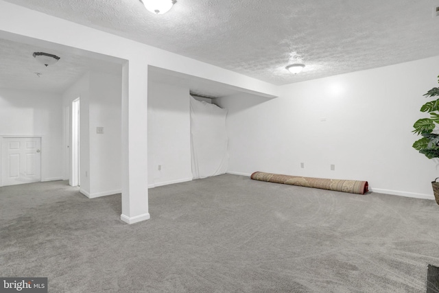 finished below grade area with a textured ceiling, visible vents, baseboards, and carpet floors