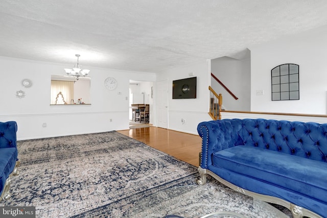 living room with a notable chandelier, crown molding, a textured ceiling, and wood finished floors