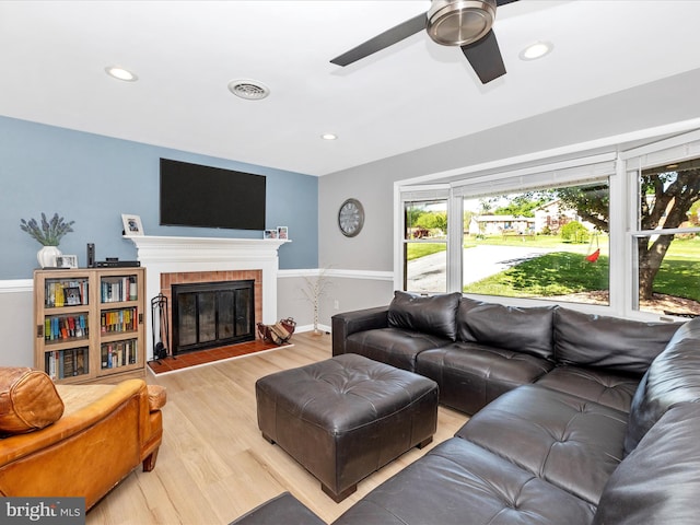 living room with a glass covered fireplace, a ceiling fan, recessed lighting, light wood-type flooring, and visible vents
