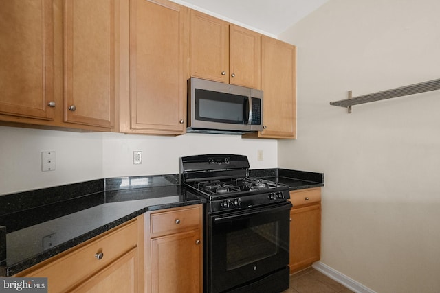 kitchen with stainless steel microwave, black range with gas stovetop, light tile patterned floors, dark stone countertops, and baseboards
