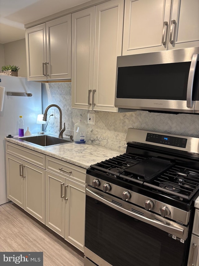 kitchen with appliances with stainless steel finishes, a sink, decorative backsplash, and light wood-type flooring