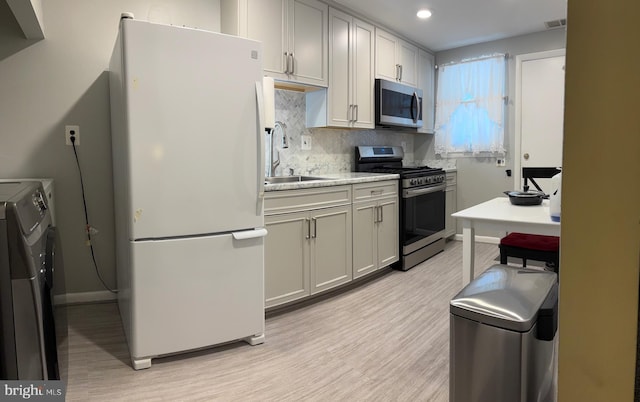 kitchen with appliances with stainless steel finishes, a sink, independent washer and dryer, light wood-style flooring, and backsplash