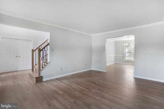 spare room featuring ornamental molding, stairs, baseboards, dark wood finished floors, and a notable chandelier