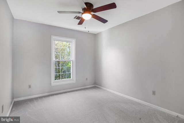 carpeted spare room featuring baseboards, visible vents, and ceiling fan