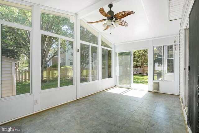 unfurnished sunroom featuring a ceiling fan, beamed ceiling, and plenty of natural light
