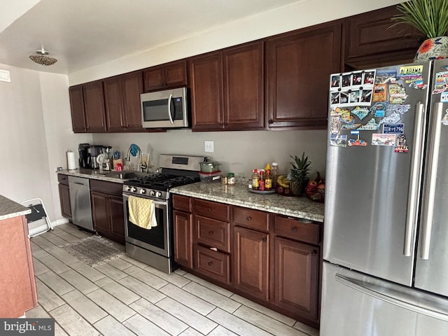 kitchen featuring light stone countertops, stainless steel appliances, dark brown cabinets, and a sink