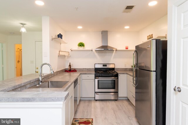 kitchen with wall chimney range hood, open shelves, a sink, stainless steel appliances, and a peninsula