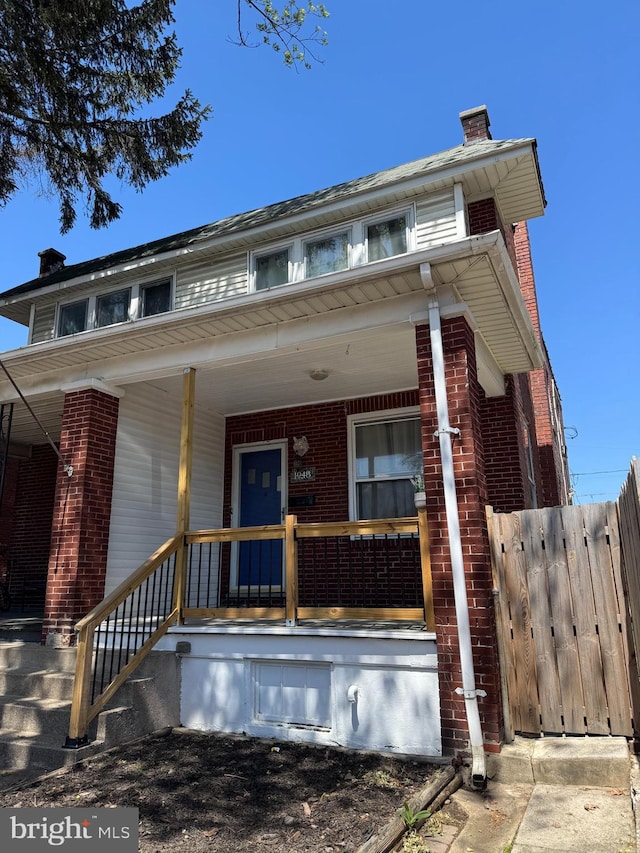 bungalow-style home with fence, a chimney, a porch, and brick siding