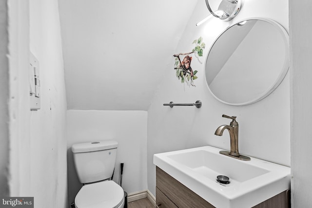 half bath featuring toilet, wood finished floors, lofted ceiling, and vanity