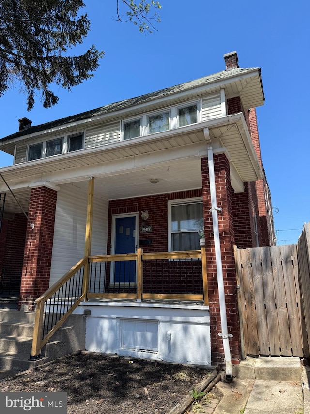 view of front of property with brick siding, fence, a chimney, and a porch