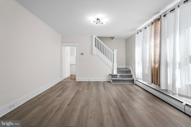unfurnished living room with wood finished floors, baseboards, stairs, and a baseboard heating unit