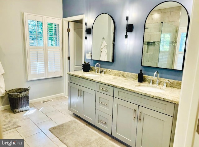 bathroom with baseboards, double vanity, tiled shower, and tile patterned flooring