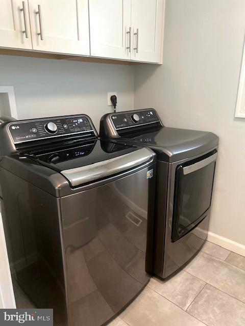 washroom featuring cabinet space, independent washer and dryer, baseboards, and light tile patterned flooring