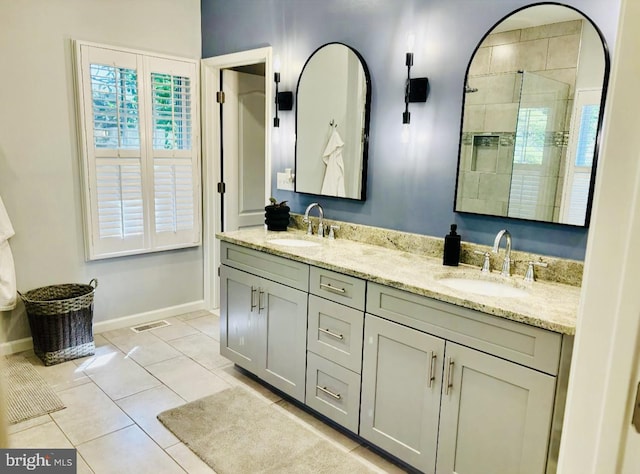 full bathroom with baseboards, double vanity, tiled shower, and tile patterned floors