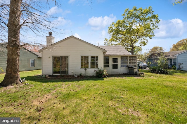 rear view of house featuring a chimney and a lawn