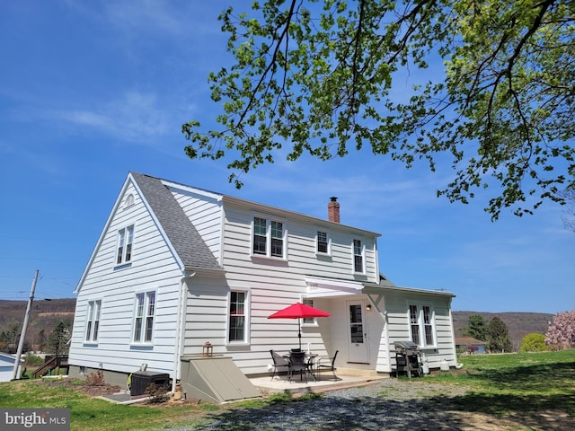 rear view of property with a chimney, cooling unit, a yard, a patio, and a shingled roof