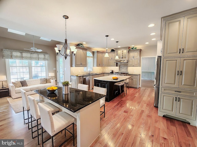 kitchen with light wood-style flooring, appliances with stainless steel finishes, a kitchen island, a sink, and a kitchen breakfast bar