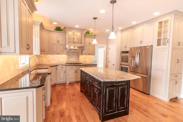 kitchen featuring glass insert cabinets, a sink, light wood-style flooring, and stainless steel appliances