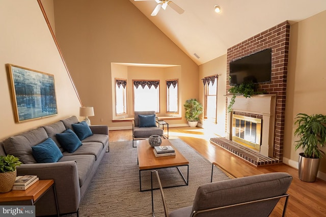 living room featuring high vaulted ceiling, wood finished floors, a ceiling fan, and a brick fireplace